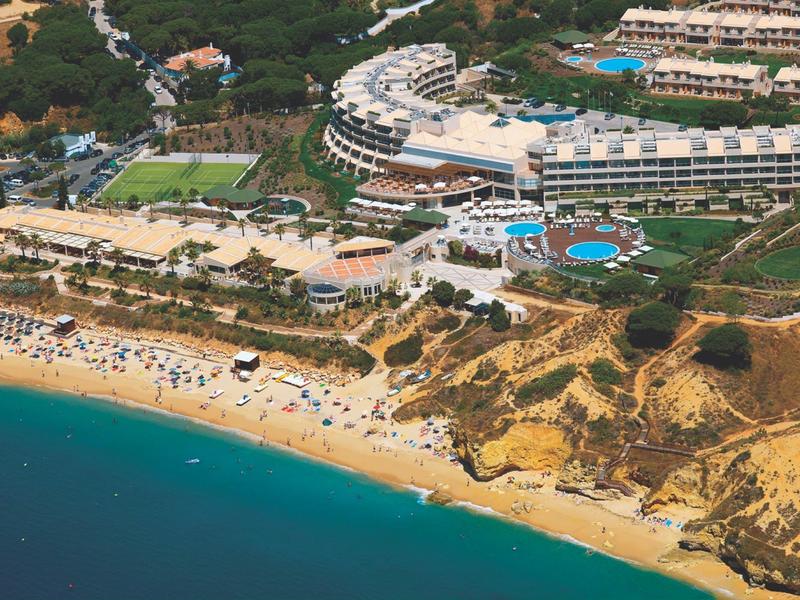 Luftaufnahme von Strand mit gelbem Sand, blauem Meer und Hotelanlage mit Pools im Hintergrund.
