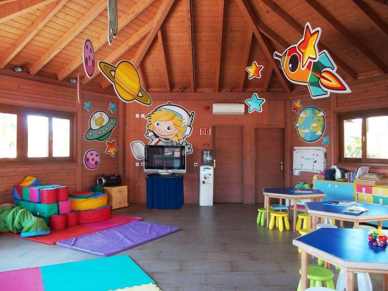 Bunter, heller Spielraum mit Holzdecke, Matten, kleinen Tischen und farbigen Weltraum-Dekorationen.