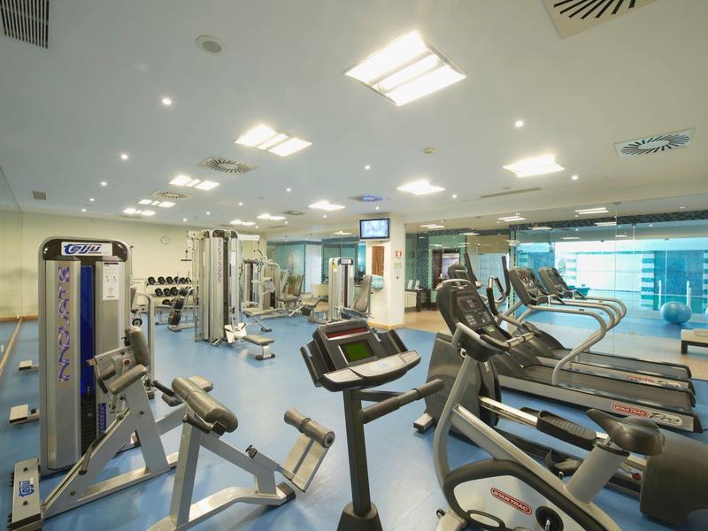 Großer, heller Fitnessraum mit modernen Geräten, Laufbändern und Spiegeln an der Wand.