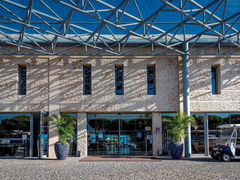 Modernes Gebäude mit großen Fenstern, steinerner Fassade und blauem Glasdach.