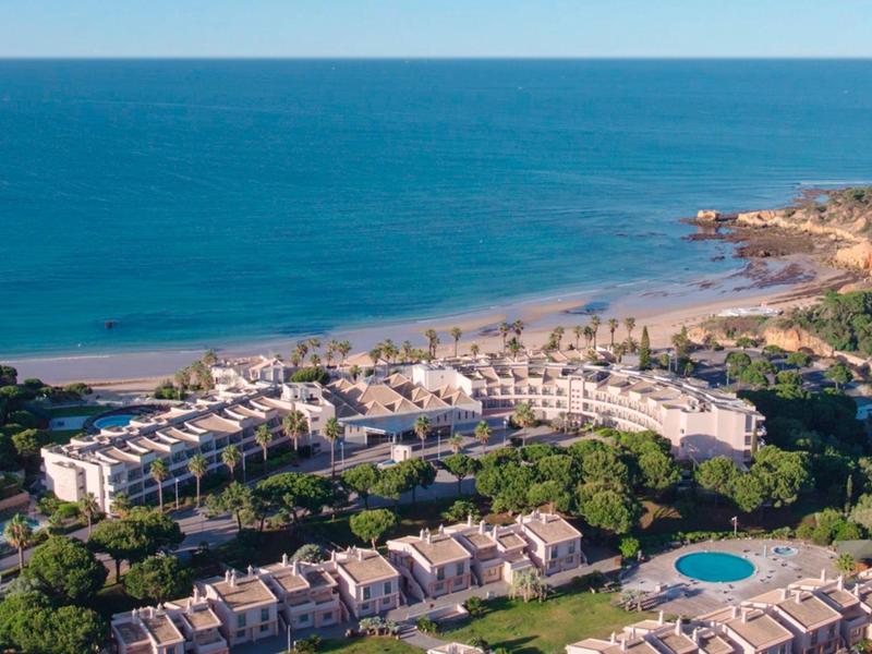 Hotelanlage mit rundem Pool an grüner Küste und weitem, blauem Meer im Hintergrund bei klarem Himmel.