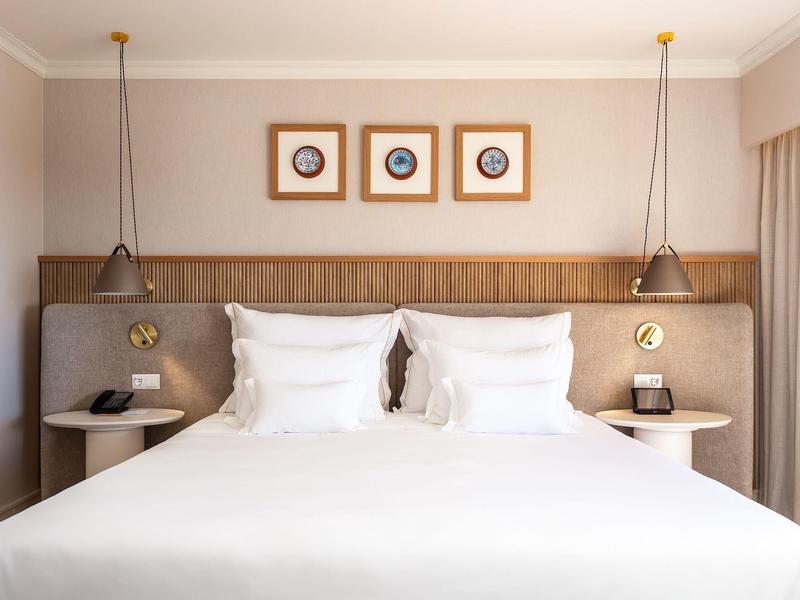 Ein großes Doppelbett mit weißen Kissen, zwei hängenden Lampen und drei gerahmten Bildern an der Wand.