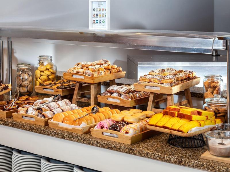 Vielfältiges Frühstücksbuffet mit Croissants, Brötchen, Kuchen und Müslivariationen auf Holzetagen.