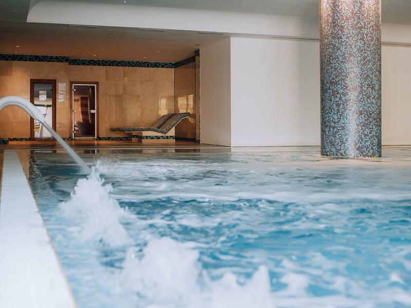 Moderner Innenpool mit Sprudelwasser, hellem Mosaikpfeiler und entspannenden Lounge-Bereichen.