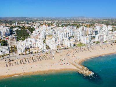 Strand mit vielen Sonnenliegen und umliegender Stadt am Meer.