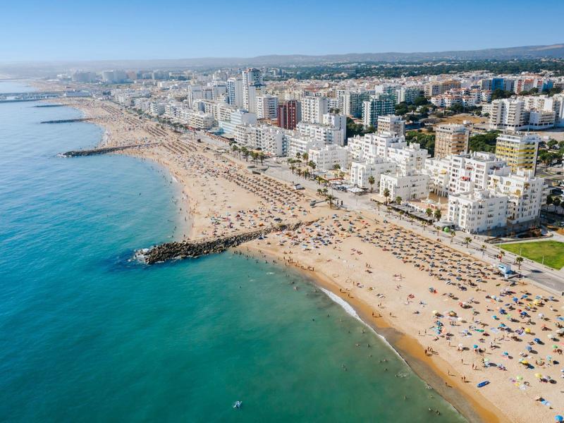Langer Sandstrand mit vielen Sonnenschirmen und hohen Gebäuden entlang der Küste bei klarem Himmel.