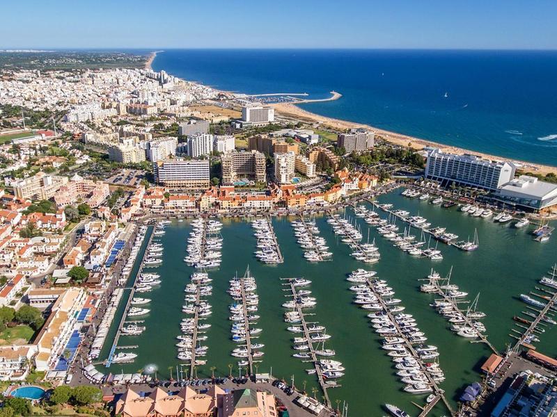 Luftaufnahme eines großen Yachthafens mit zahlreichen Booten, umgeben von Stadt und blauem Meer.