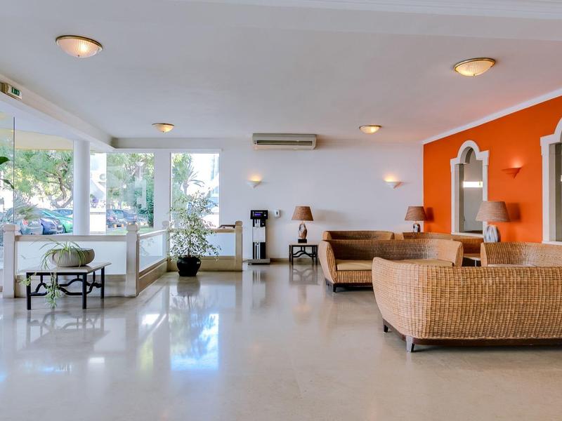 Großes, helles Wohnzimmer mit weißen Wänden, oranger Akzentwand, Rattansofas und großem Fenster.