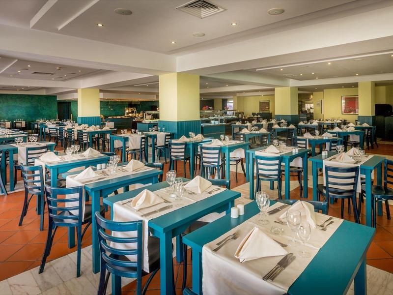 Przestronna sala restauracyjna z nakrytymi stołami i niebieskimi krzesłami.