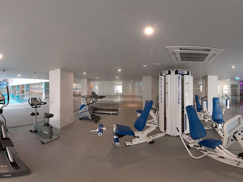 Nowoczesna siłownia z różnym sprzętem, bieżniami i maszynami do ćwiczeń.