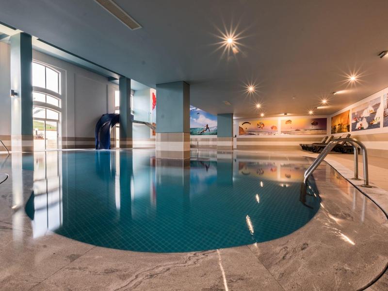 Kryty basen z marmurową podłogą i ścianami ozdobionymi zdjęciami krajobrazów.