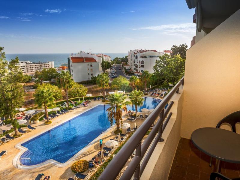 Widok na basen otoczony palmami z nasłonecznionego hotelowego balkonu.