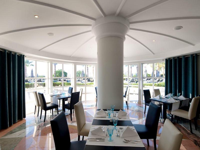 Jasna sala restauracyjna z nakrytymi stolikami i dużymi okrągłymi oknami.