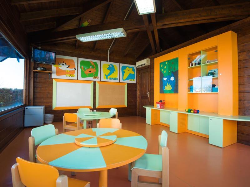 Sala zabaw dla dzieci z kolorowymi stolikami i jasnymi dekoracjami na ścianach.