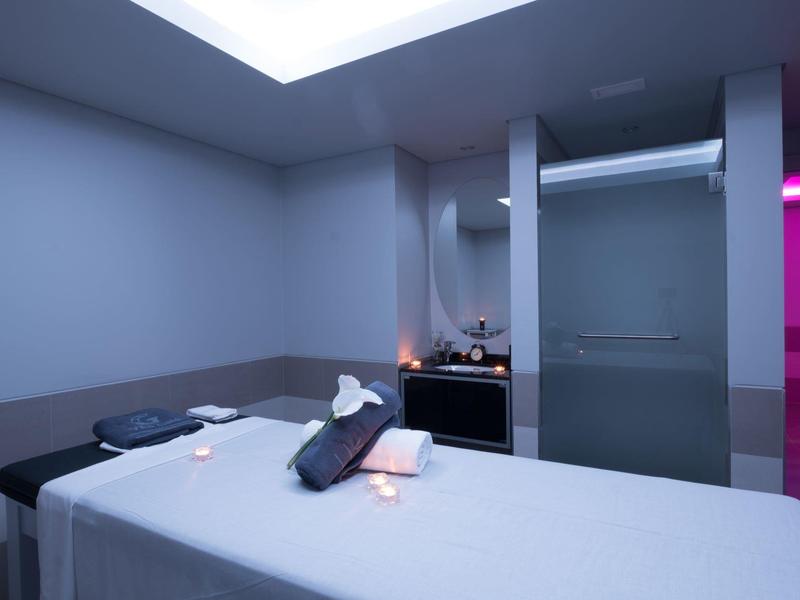 Pokój do masażu z łóżkiem, ręcznikami i przygaszonym światłem.