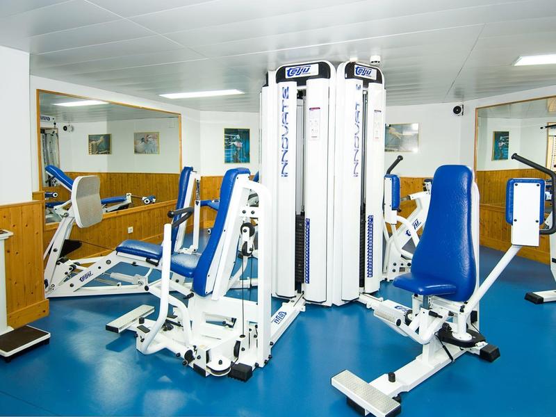 Siłownia z urządzeniami do ćwiczeń siłowych, niebieskie siedzenia i podłoga.