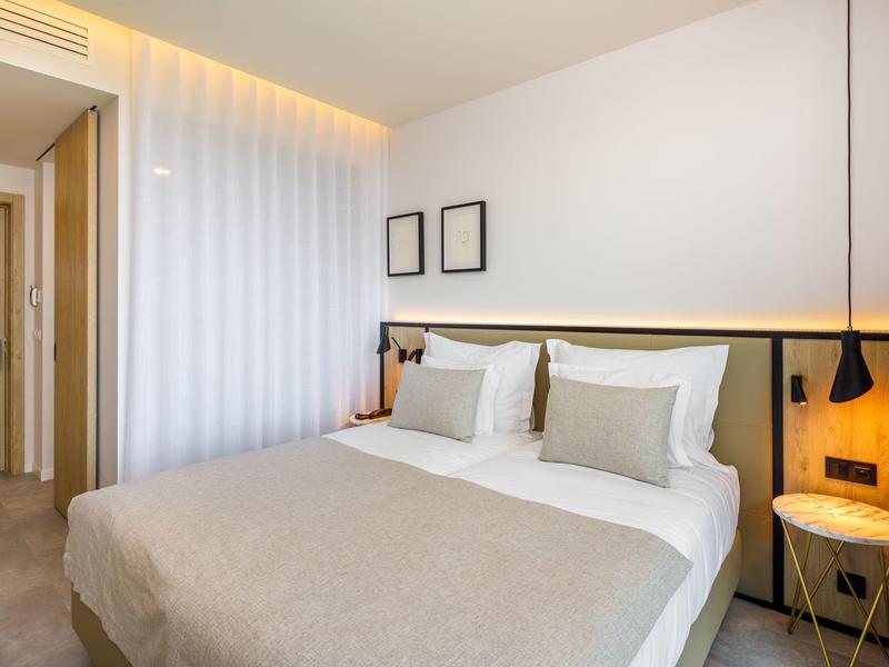 Moderne slaapkamer met tweepersoonsbed, neutrale kleuren en minimale decoratie in een hotelkamer.