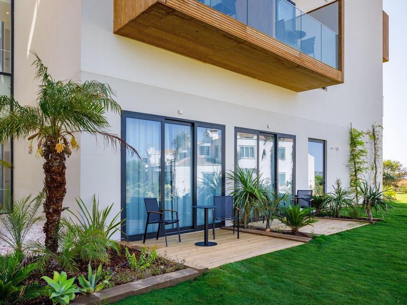 Moderne hotelterras met glazen balkons, groene planten en goed onderhouden gazon.