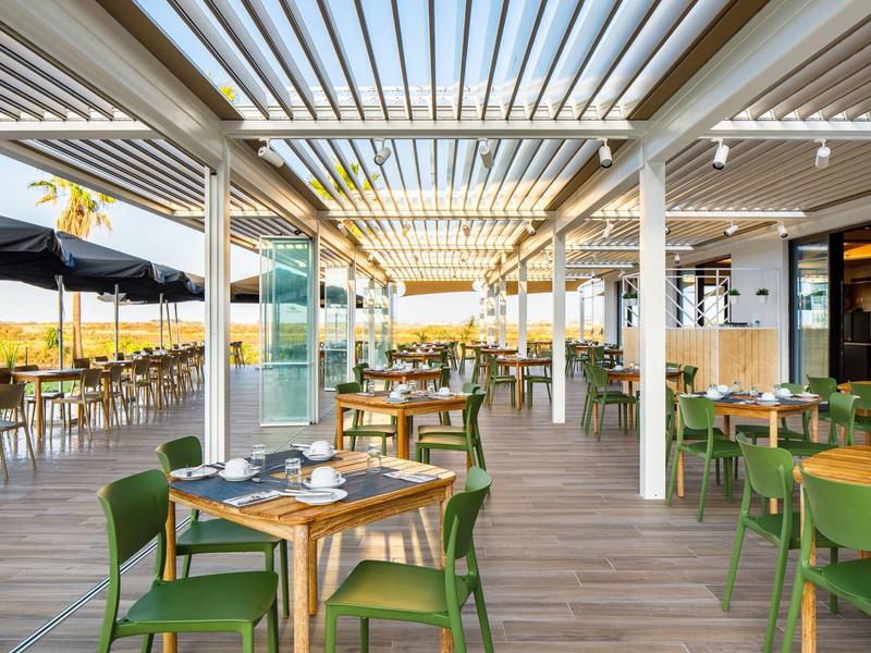 Open restaurant met houten vloer, groene stoelen en modern ontwerp onder een lattendak.