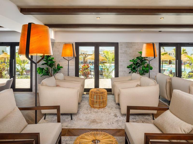 Knusse lounge met comfortabele fauteuils, warm licht en planten bij grote ramen.