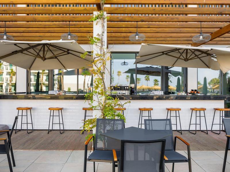Moderne buitenbar van hotel met krukken, tafels, stoelen en parasols.
