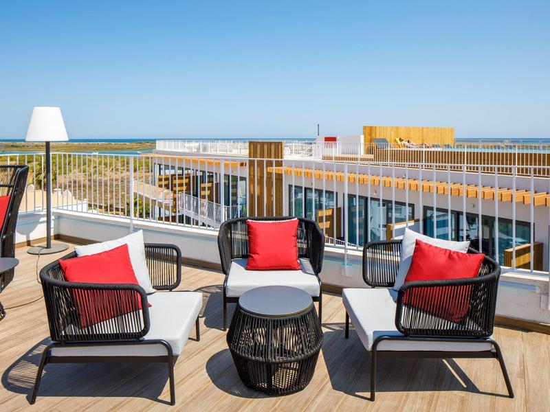 Moderne terrasmeubels met rode kussens op een hotelverdieping met uitzicht op zee en een heldere lucht.