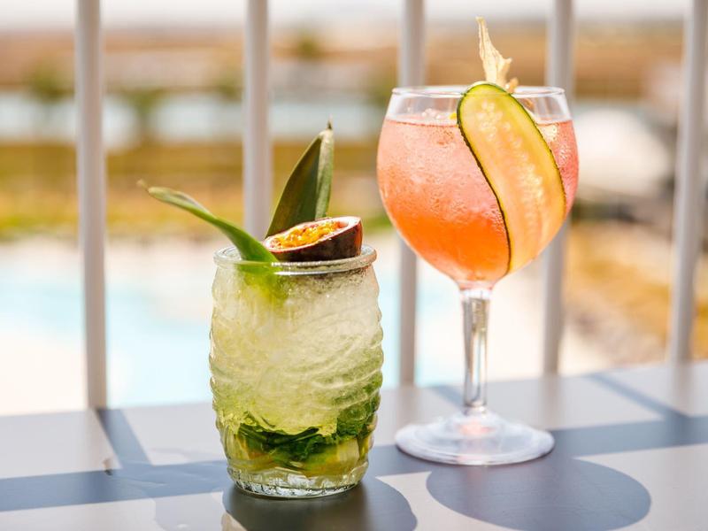 Twee kleurrijke cocktails op een tafel met een vervaagde terrasachtergrond.