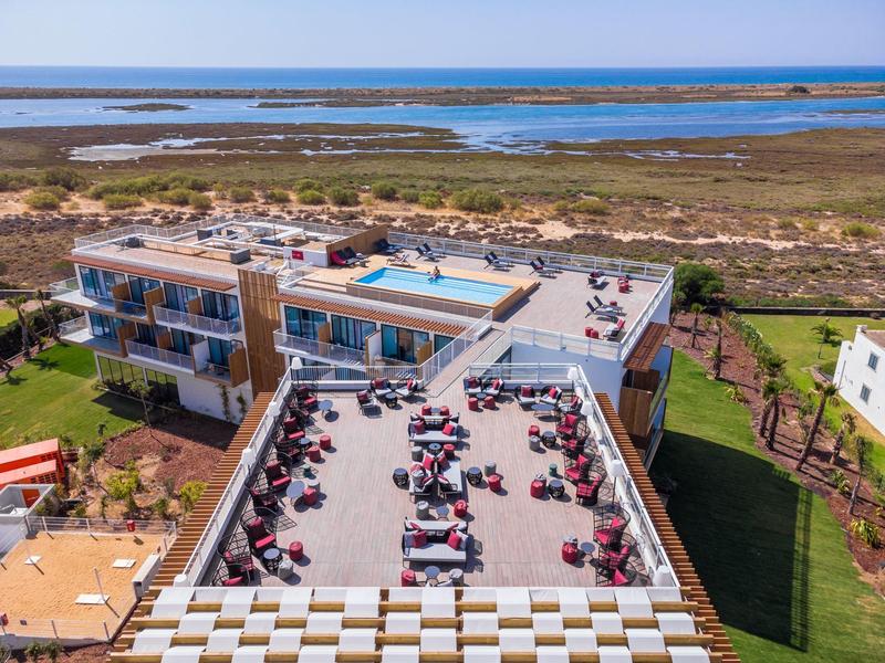 Modern hotelcomplex met meerdere gebouwen, terras met tafels en uitzicht op het kustlandschap.