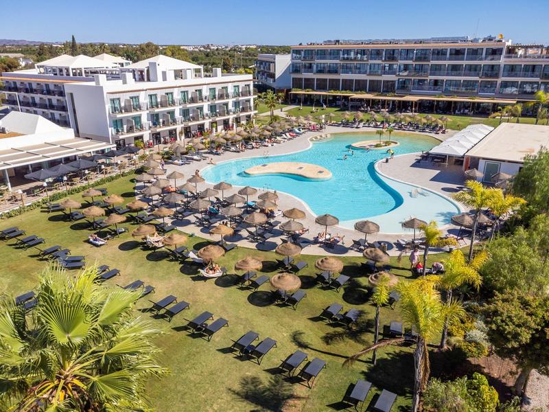 Groot hotelresort met een gebogen buitenzwembad, ligbedden en parasols in de tuin.