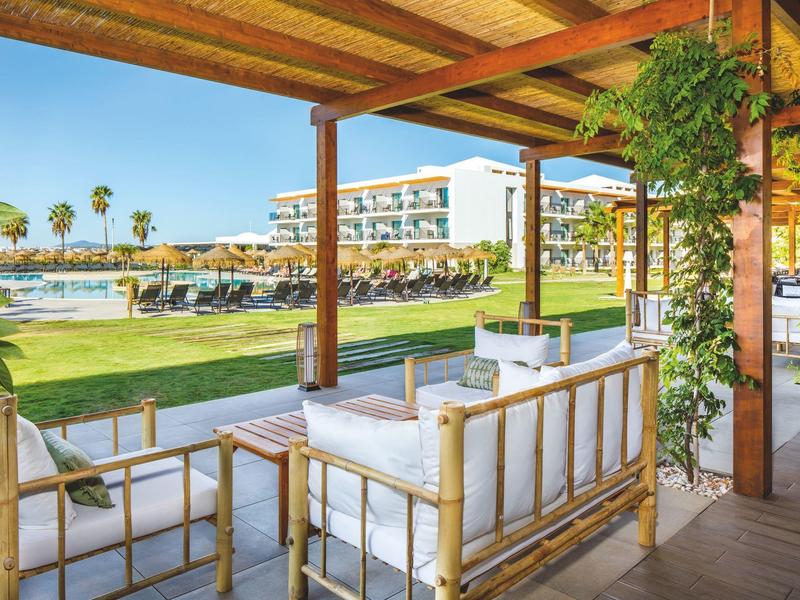 Overdekt terras met zitplaatsen en uitzicht op een zwembad en hotelgebouwen.