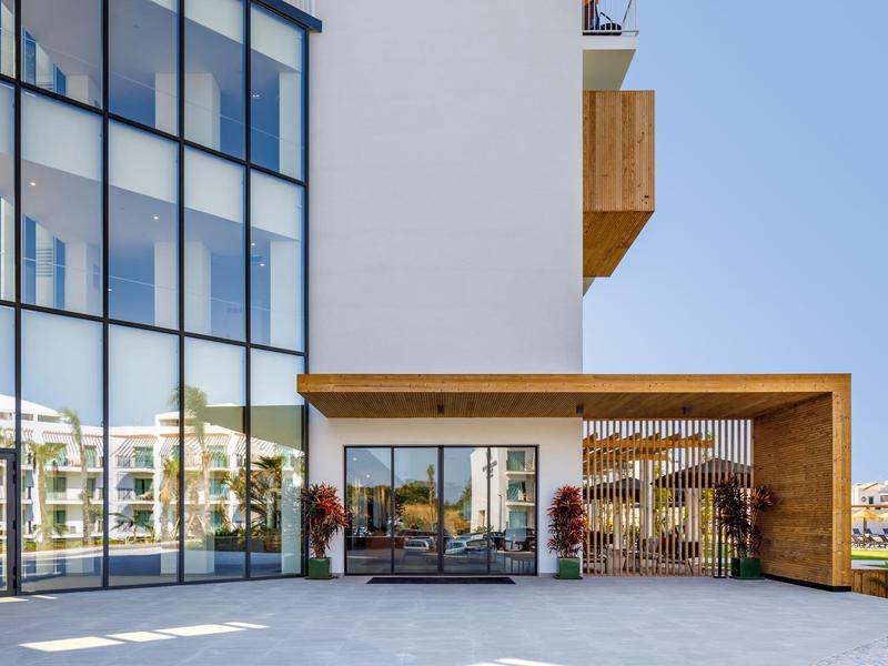 Moderne hotelfront met grote ramen en gezellige zithoeken onder een heldere hemel.