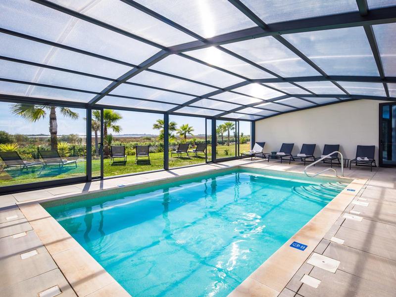 Modern overdekt zwembad met ligstoelen en uitzicht op tropische tuin.