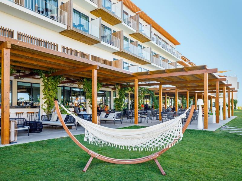 Gezellige hangmat op groen gras voor een modern hotel met terras en zitplaatsen.