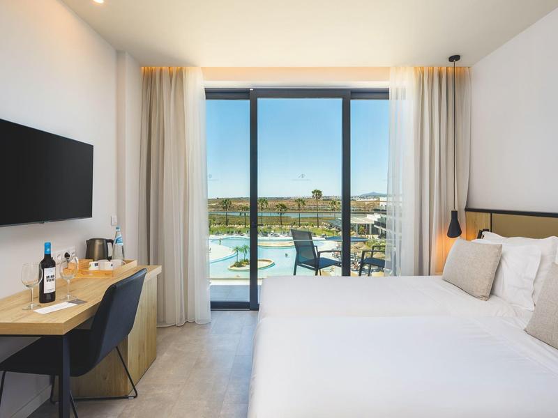 Moderne hotelkamer met tweepersoonsbed, bureau, tv en balkon met uitzicht op de stad.