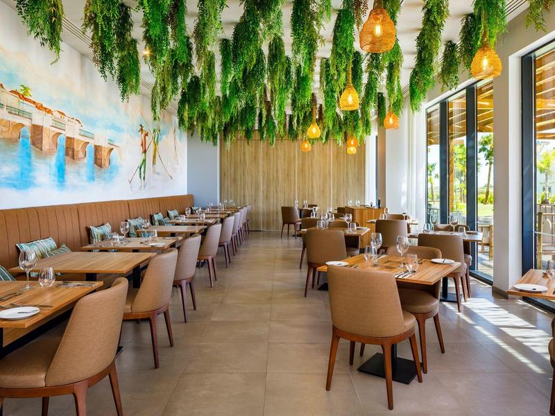 Modern restaurant met hangende groene planten en warme verlichting naast grote ramen.