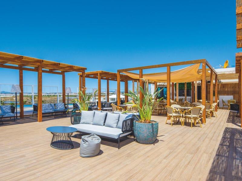 Moderne terras met loungeset en eethoek bij zonnig weer aan het water.