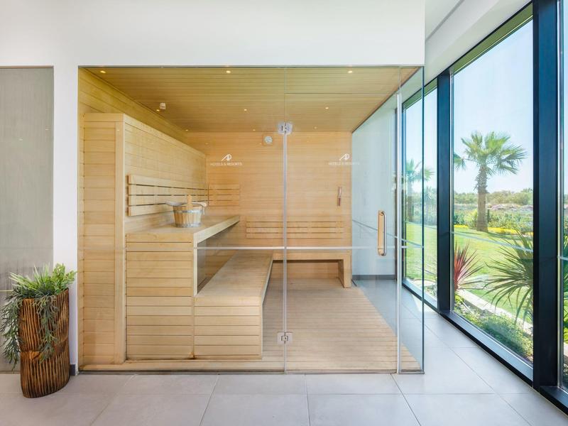 Moderne sauna met glazen voorzijde en uitzicht op groene tuin en palmbomen.