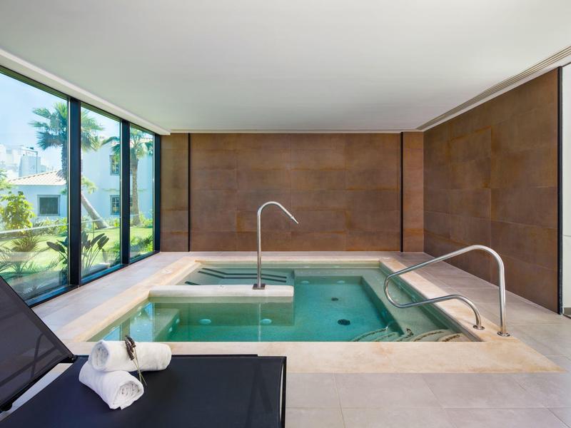 Moderne binnenzwembad met grote glazen ramen en een ontspannen zwarte ligstoel.