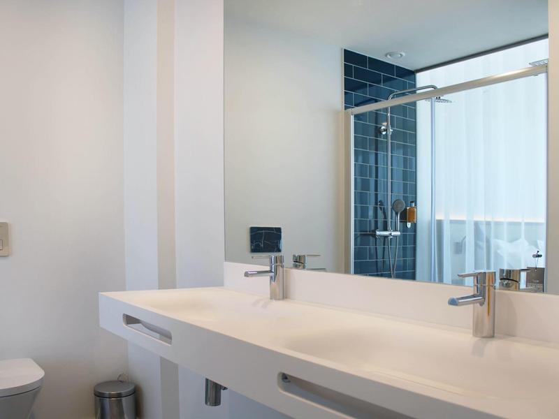 Moderne hotelbadkamer met twee wastafels en aparte douche met glazen wand.