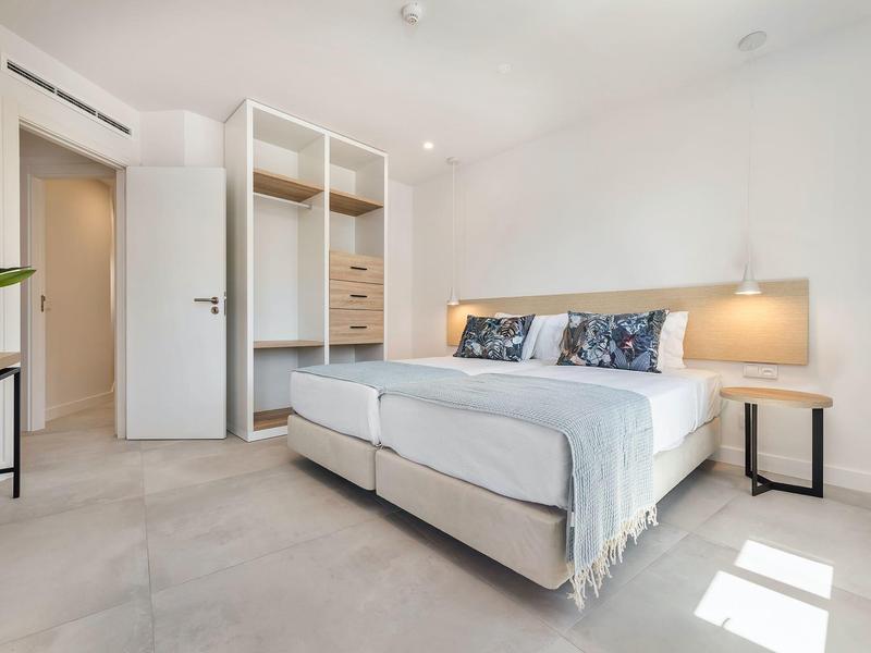 Nowoczesna sypialnia z podwójnym łóżkiem, otwartą szafą i minimalistyczną szafką nocną.