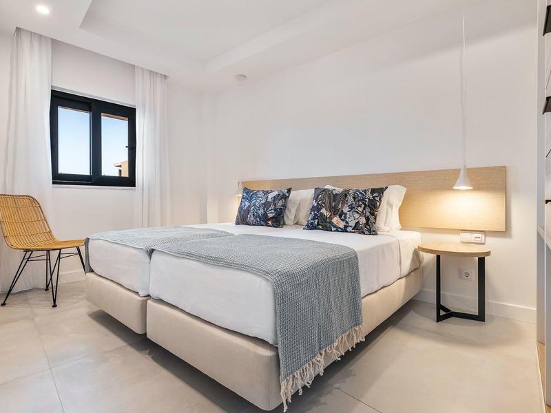 Jasno urządzone sypialnia z podwójnym łóżkiem, krzesłem i lampką nocną.