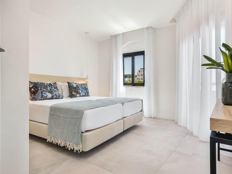 Jasny pokój hotelowy z dwoma pojedynczymi łóżkami, oknami i minimalistycznym wystrojem.