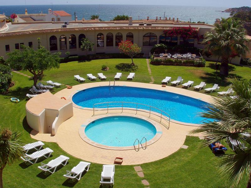 Ogród hotelowy z dwoma basenami, leżakami i widokiem na morze.