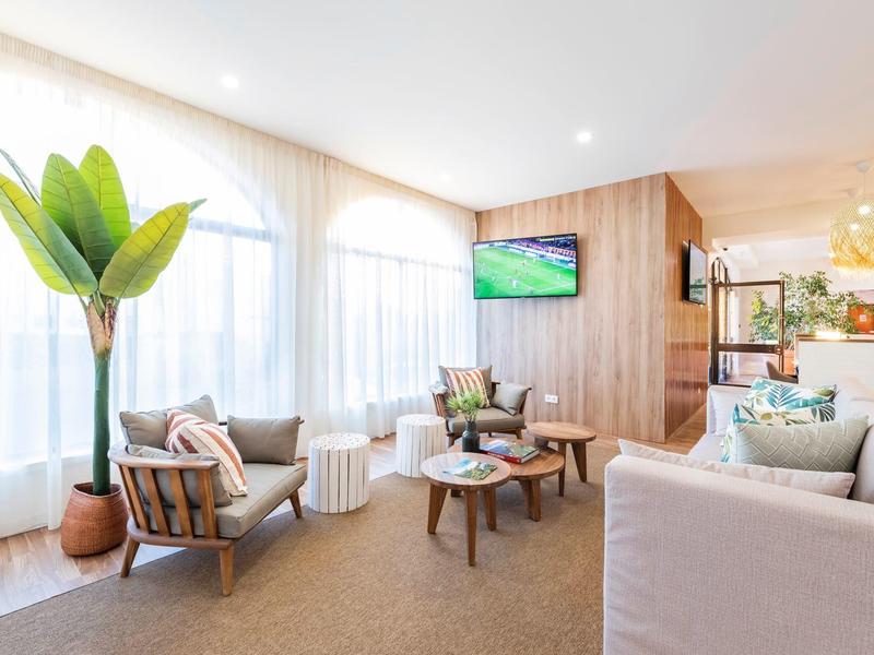 Jasny, nowoczesny pokój hotelowy z dużymi oknami, roślinami i wygodnymi miejscami do siedzenia.