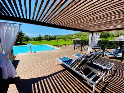 Überdachte Terrasse mit Liegestühlen und Blick auf einen Pool und grüne Landschaft.