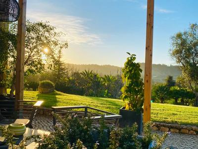 Sonnige Terrasse mit Holzbalken, Blick auf Garten und Hügel bei Sonnenuntergang.