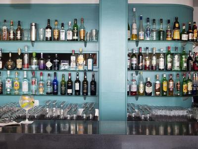 Moderne hotelbar met diverse drankflessen op glazen planken en toonbank met drankjes.