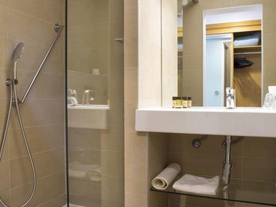 Moderne hotelbadkamer met glazen douche, grote wastafel en houten vloer.