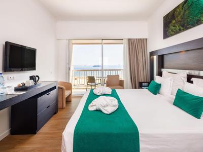 Habitación de hotel con cama doble, balcón y vista al mar en diseño moderno y luminoso.