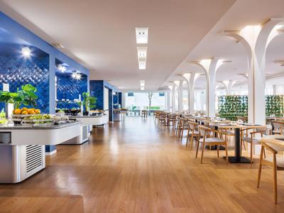 Restaurante moderno con suelo de madera, área de buffet y filas de mesas en una habitación luminosa.